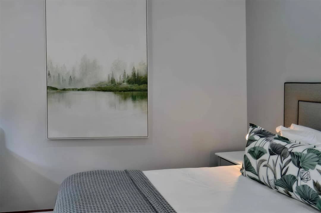 Bedside view with forest-lake artwork and leaf-patterned cushion on bed.