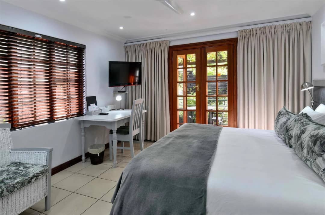 Bedroom with wooden blinds, desk, TV, and garden-facing French doors.
