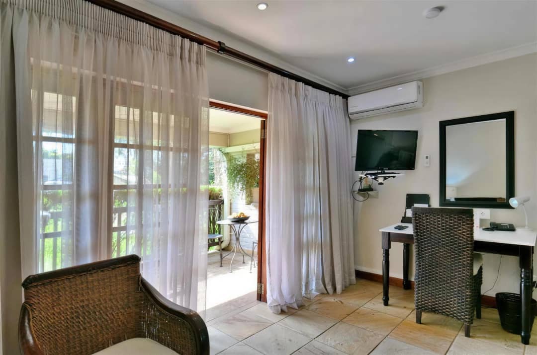 Room with desk, TV, wicker chairs and private balcony access.