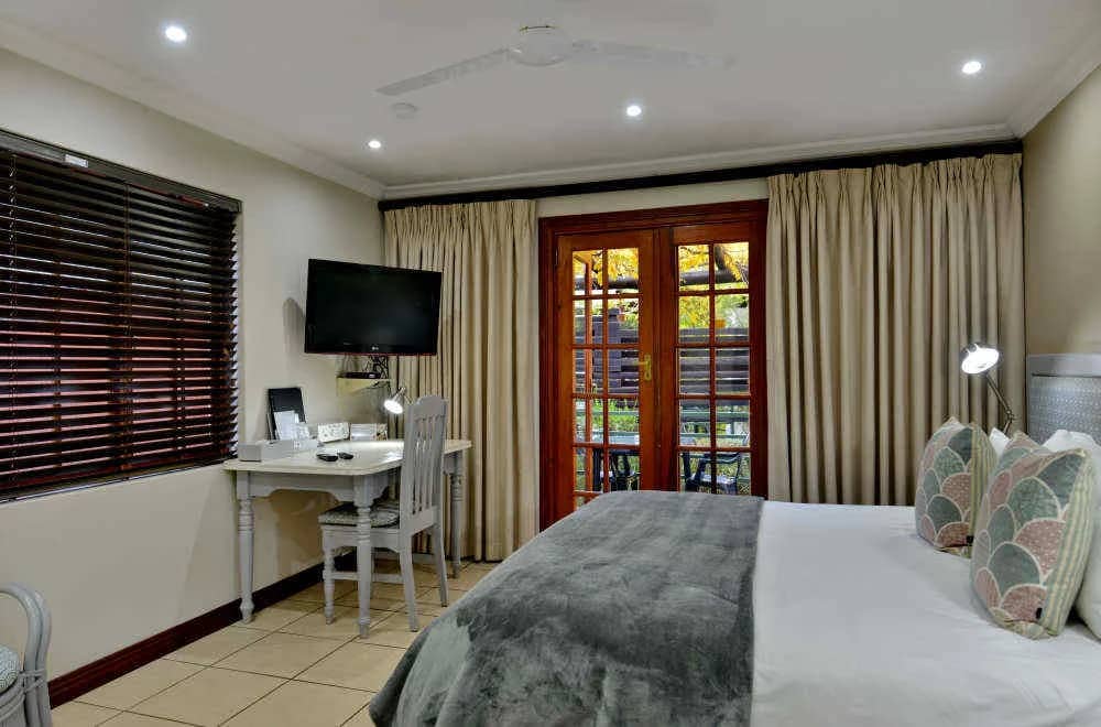 Standard room with a king bed, writing desk, wall-mounted TV and French doors to the garden